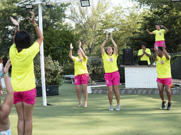 Menschen tanzen im Freien in gelben Shirts und rosa Shorts.